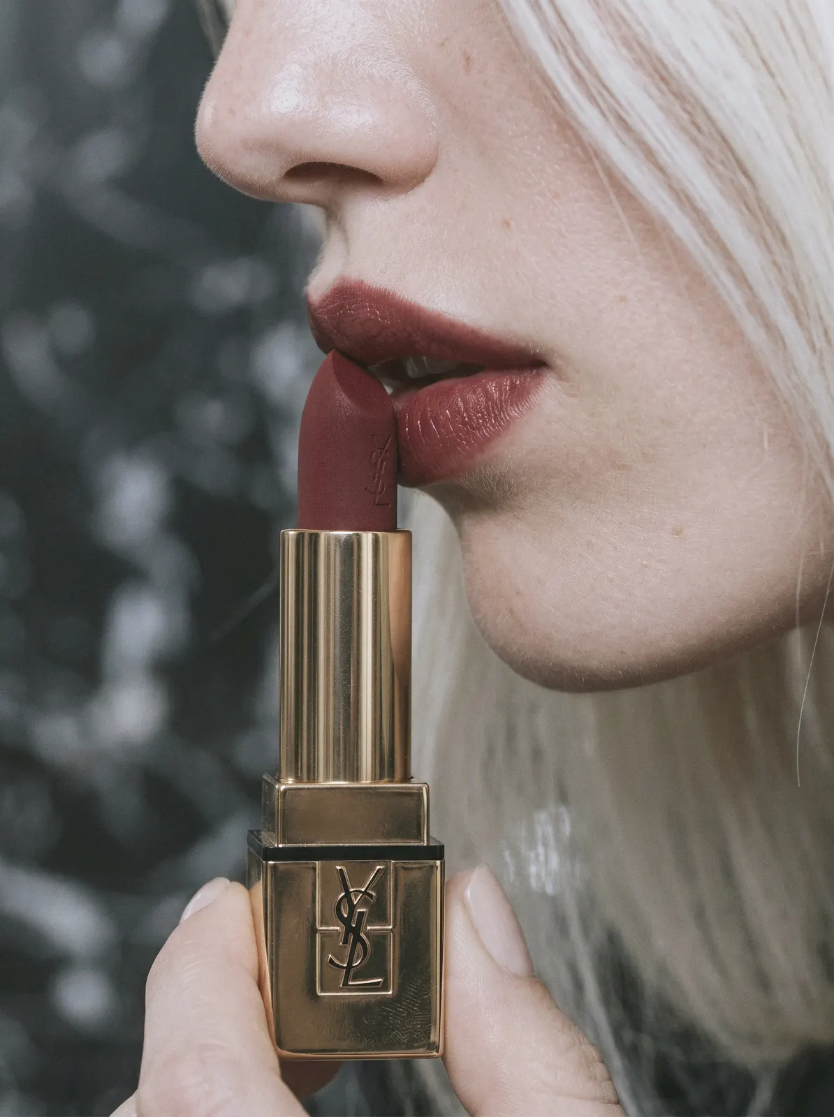 Primer plano de una modelo pintándose los labios con una barra de YSL